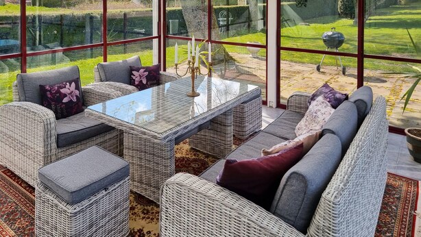 A sunlit room with wicker furniture, a glass table, and a view of a garden through large windows. - Cozy home in Svedala with WiFi (Svedala)