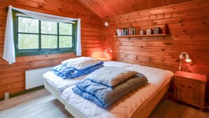 Une chambre à coucher dans une cabane en bois, avec un lit, une fenêtre, une étagère remplie de livres et une table de chevet avec une lampe.
