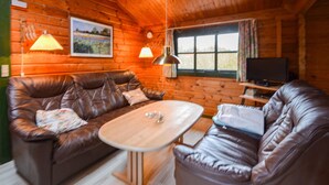 L’intérieur chaleureux d’un chalet avec un canapé en cuir marron, une table basse en bois et un téléviseur posé sur un meuble en bois.