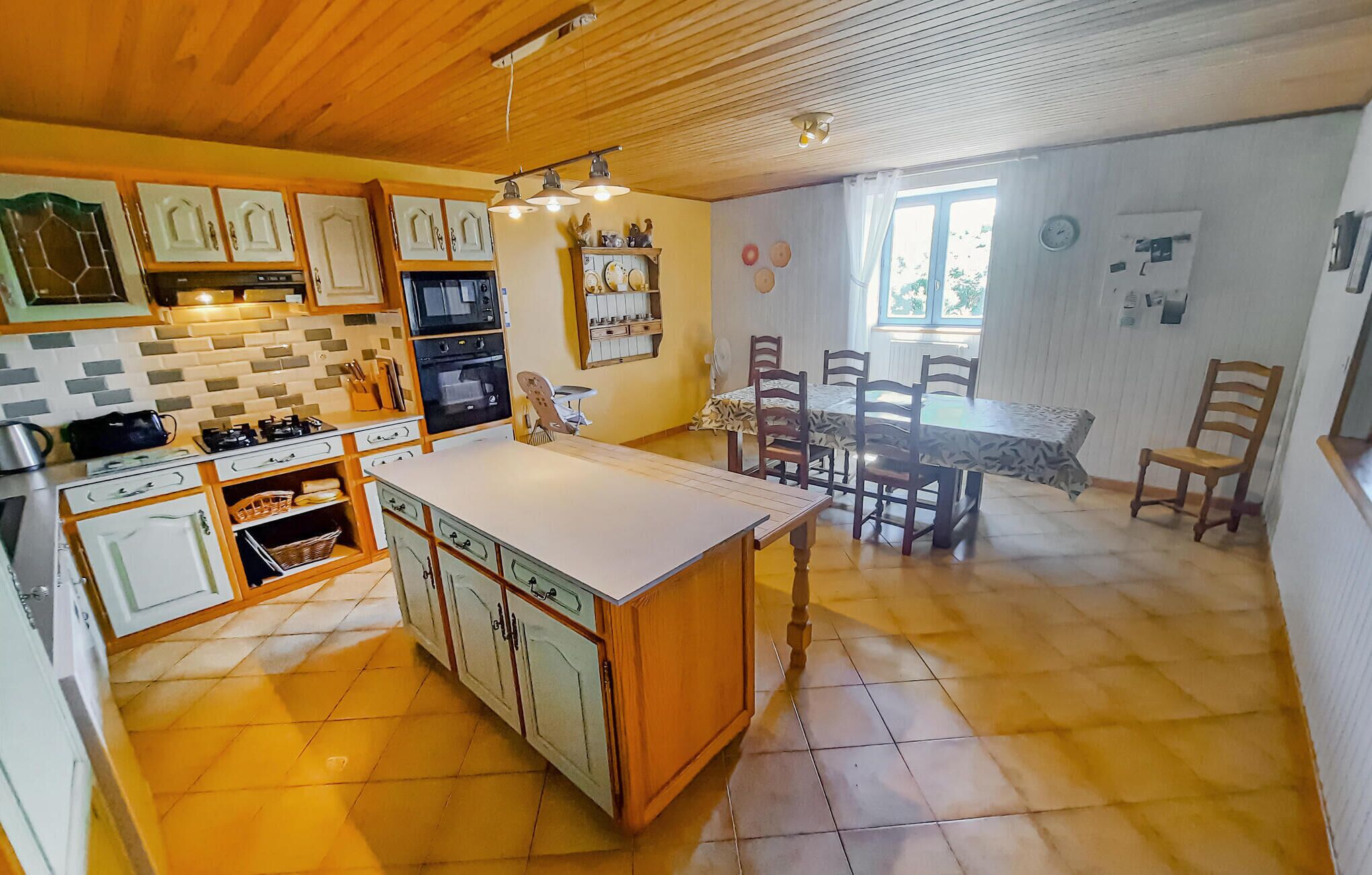 A kitchen with a central island, wooden cabinets, and a dining area with a table and chairs.