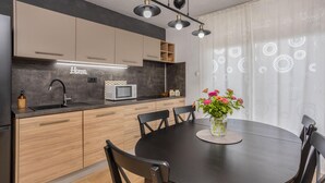 A modern kitchen with a dark countertop, wooden cabinets, and a built-in microwave. There is a dining table with chairs and a vase of flowers.