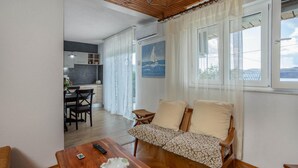 A cozy living room with a wooden sofa, a dining table, and a kitchen area in the background.
