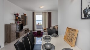 A modern living room with a dining area, a wooden cabinet, and a view of the sea.