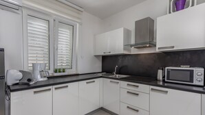 A modern kitchen with white cabinets, a black countertop, a stainless steel sink, and a microwave.