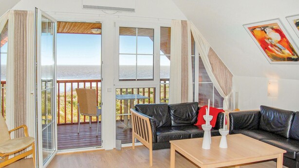 Ein Zimmer mit einem schwarzen Ledersofa, einem Holztisch und Meerblick durch große Glasfenster.
