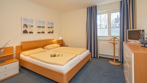 Un dormitorio con una cama de madera, una mesita de noche, un escritorio con computadora y una ventana con cortinas.