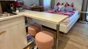 Habitación de hotel compacta con kitchenette, una cama con colcha estampada, una pequeña mesa de comedor y una silla.