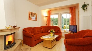 A living room with a fireplace, orange sofa, wooden coffee table, and a television. - Usedom tourist Koserow Hauptstr. DHH 14 - DHH 14 (Koserow)