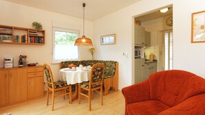 A dining area with a table set for four, surrounded by chairs. There is a red armchair to the right. A bookshelf with books and a small plant is on the left. A window provides natural light. - Usedom tourist Koserow Hauptstr. DHH 14 - DHH 14 (Koserow)