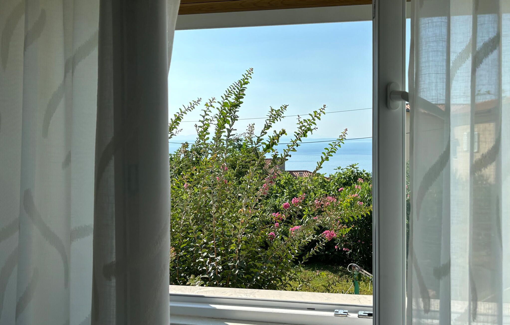 Uitzicht door een raam op een tuin en de zee.