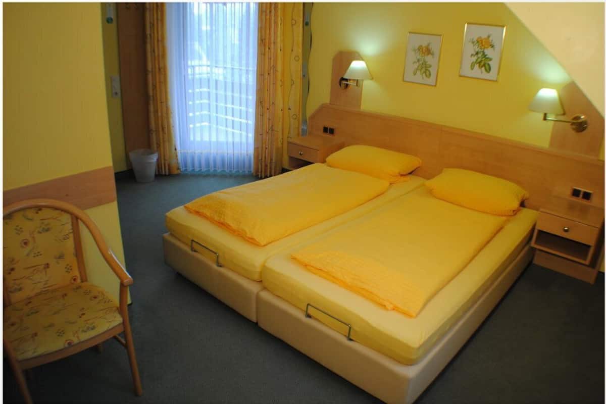 Una cama doble con dos almohadas, una silla, una mesita de noche y una lámpara.