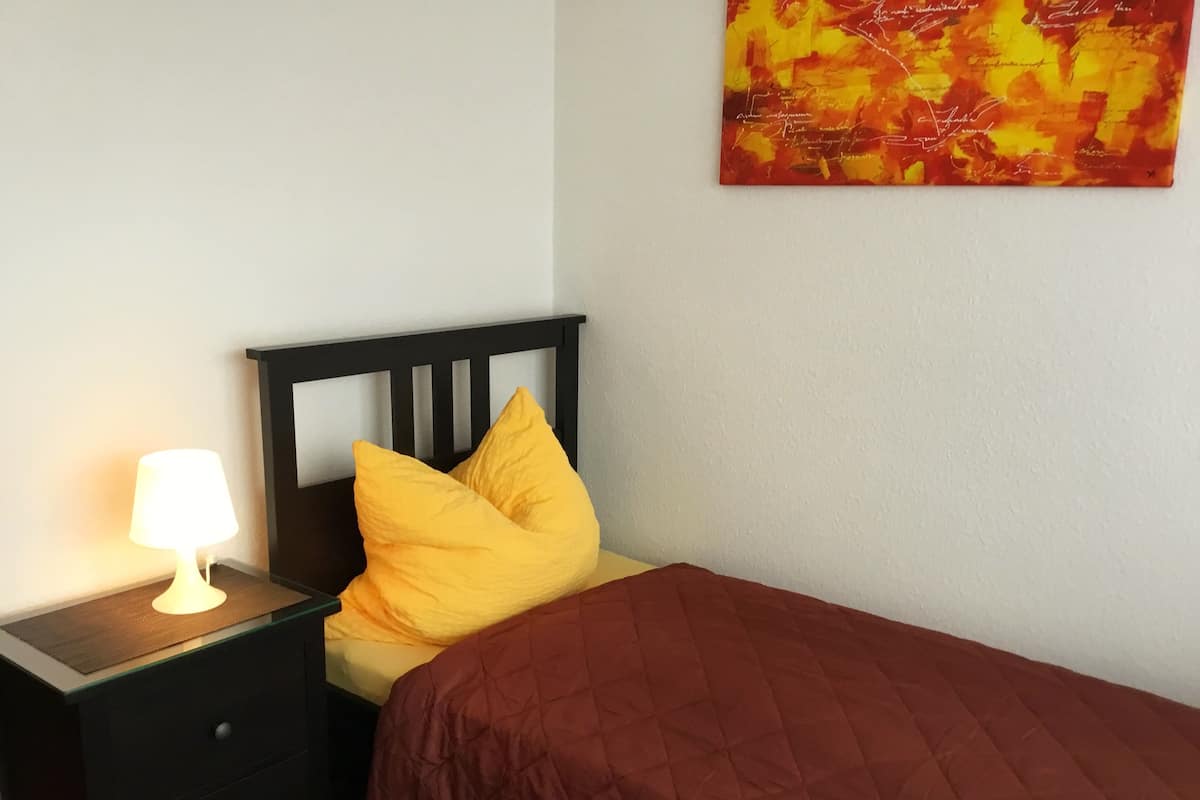 Un dormitorio con cama, mesita de noche, lámpara y un cuadro en la pared.
