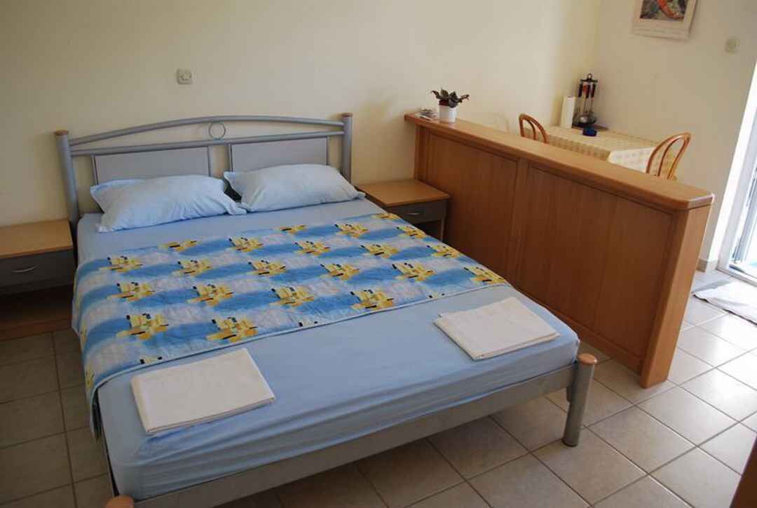 A single bed with a blue and yellow patterned bedspread, a wooden nightstand, a wooden dresser, and a small table with a chair.