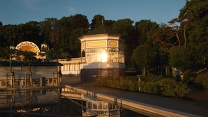 Un gazebo con tetto in vetro, circondato da un elemento d'acqua e vegetazione.