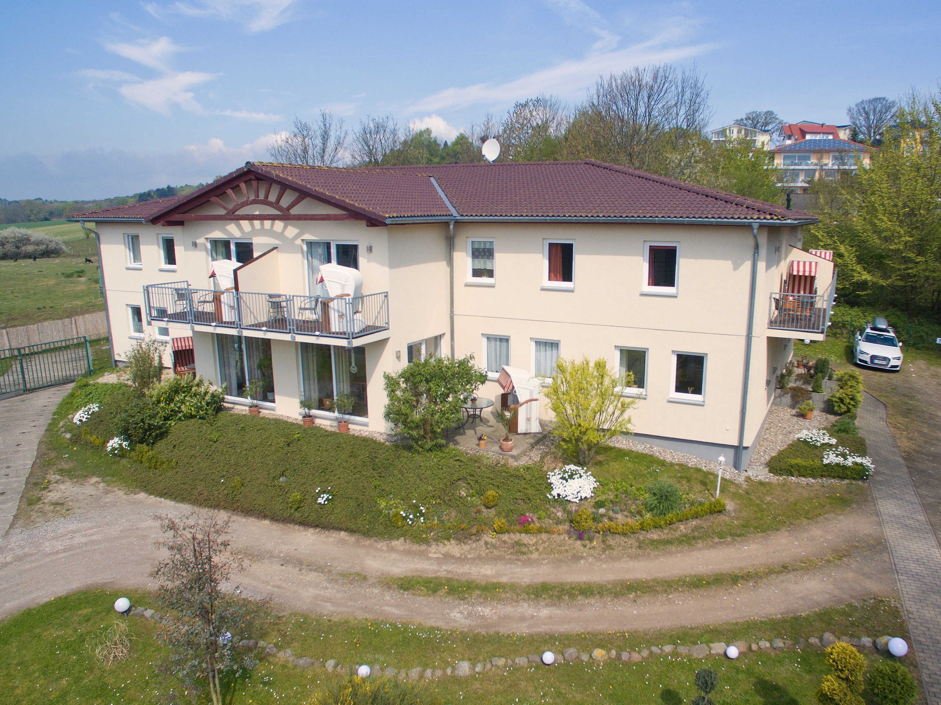 Ein zweistöckiges Gebäude mit Balkon, Auffahrt und einem Garten mit verschiedenen Pflanzen und Blumen.
