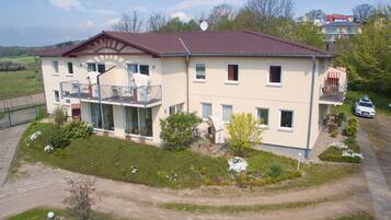 Ein zweistöckiges Gebäude mit Balkon, Auffahrt und einem Garten mit verschiedenen Pflanzen und Blumen.