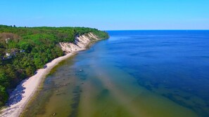 A coastal landscape with a sandy beach, clear blue water, and a forested cliff. - Beach Chair House 8, Ocean View, 150 m from the Beach (Göhren)