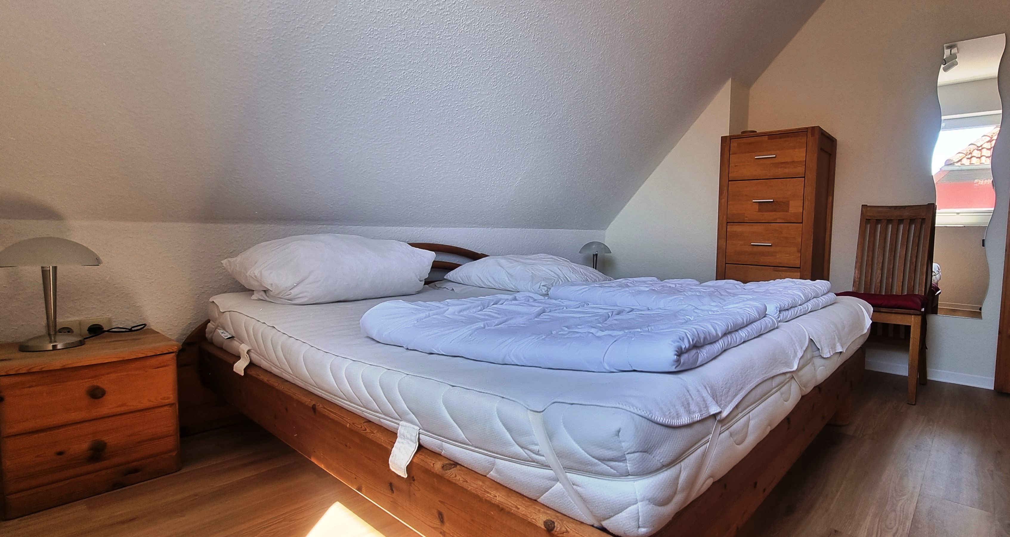 Une chambre à coucher avec un lit en bois, une table de chevet avec une lampe, une armoire en bois et une chaise.