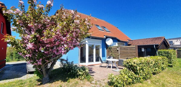 A house with a red roof, a garden with flowering trees, and a patio with outdoor furniture.