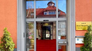 A hotel entrance with a red carpet, a glass facade, and a sign indicating the hotel's name and contact number. - Triple Room - Hotel Burgschmiet GmbH (Nürnberg)