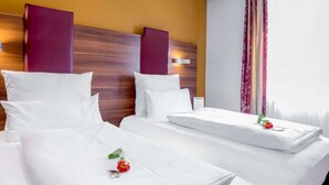 A hotel room with two beds, each with white linens and pillows, a wooden headboard, and a window with curtains. - Triple Room - Hotel Burgschmiet GmbH (Nürnberg)