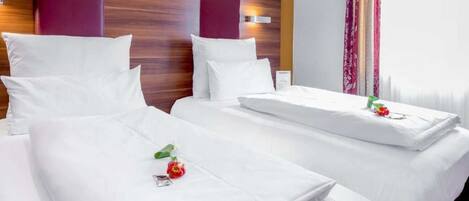Habitación de hotel con dos camas, cada una con ropa de cama y almohadas blancas, cabeceros de madera y una ventana con cortinas.