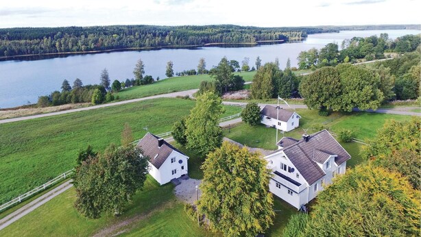 A large white house with a dark roof, surrounded by lush green fields and trees, near a lake. - Beautiful home in Dalum with kitchen (Dalum)