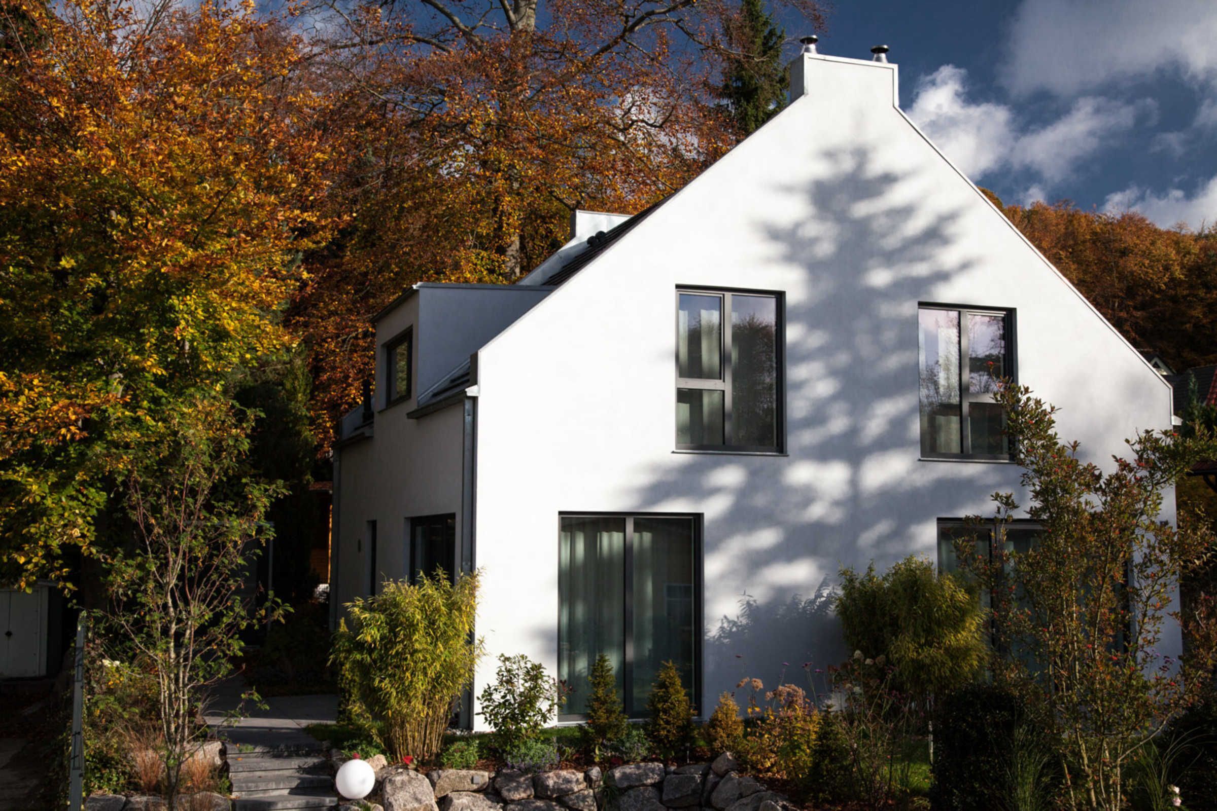 Et moderne hvidt hus med et stejle tag, omgivet af efterårsblade og en stenkø ved indgangen.