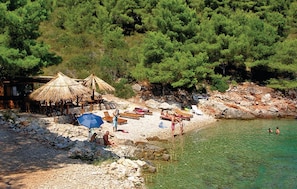 A beach with thatched umbrellas, sun loungers, and a rocky shoreline.