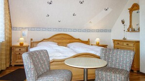 A bedroom with a wooden bed, two bedside tables with lamps, a round table with two patterned chairs, and a mirror on the wall.