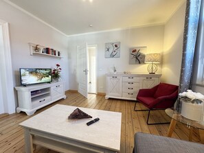 A modern living room with a TV, a red chair, a glass table, and a white cabinet.
