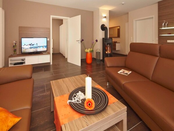 Un salon moderne avec un canapé, une table basse sur laquelle est posée une bougie et un téléviseur.