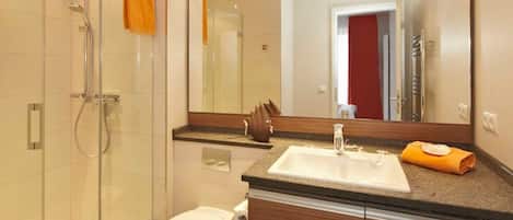A modern bathroom with a glass shower enclosure, a white toilet, a large mirror, and a wooden vanity.