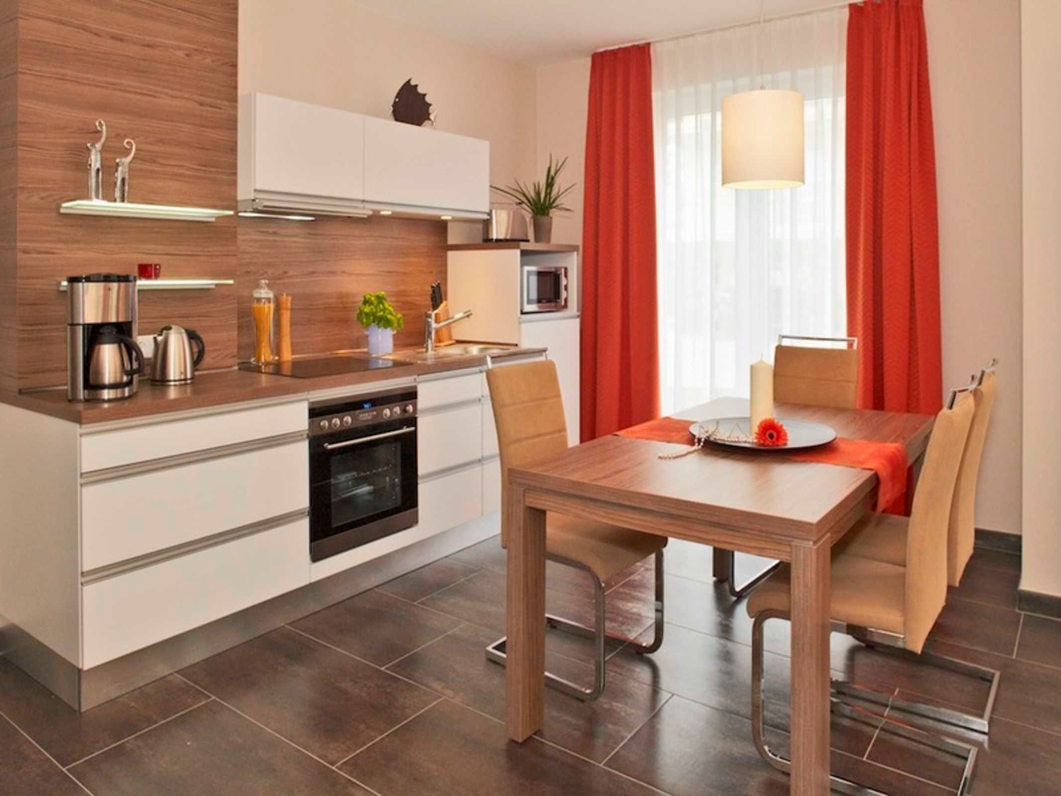 A modern kitchen with a central island, a dining area with a wooden table and chairs, and a window with red curtains.