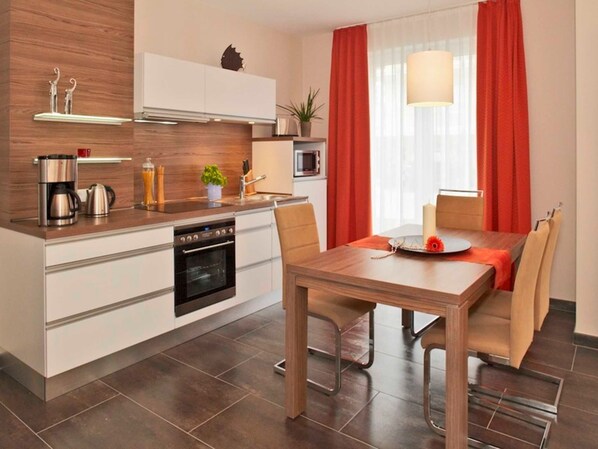 Une cuisine moderne avec un îlot central, un coin repas avec une table et des chaises en bois, et une fenêtre agrémentée de rideaux rouges.