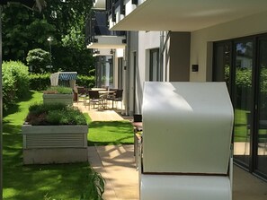 Un espace extérieur moderne doté d’une terrasse, de coins salon et d’un chemin menant à un bâtiment aux grandes fenêtres.