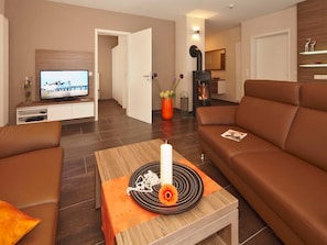 Un salon moderne avec un canapé, une table basse sur laquelle est posée une bougie et un téléviseur.