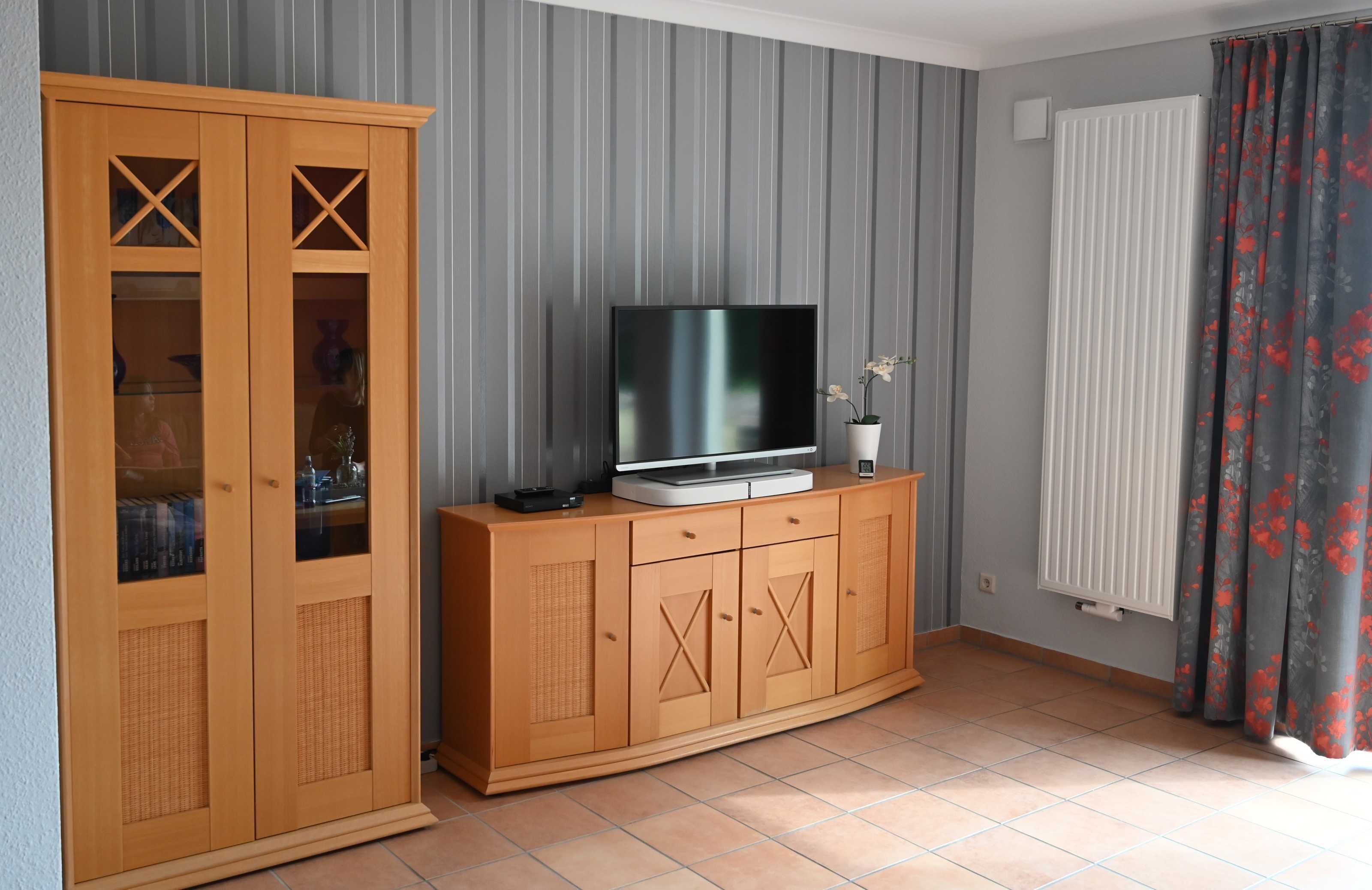 A living room with a TV on a wooden cabinet, a radiator, and striped wallpaper.