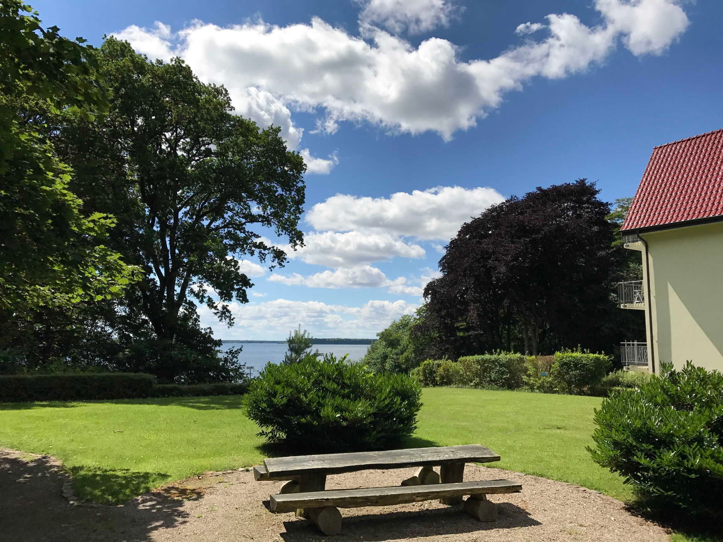 A picnic table in a grassy area with a view of the sea and a building with a red roof.