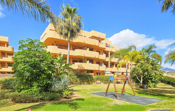 A multi-story hotel with balconies, surrounded by lush greenery and a swing set.