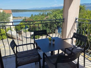 A balcony with a table and chairs, a view of a lake, and a mountain range in the background. - Holiday apartment near the beach with sea view (Klimno)