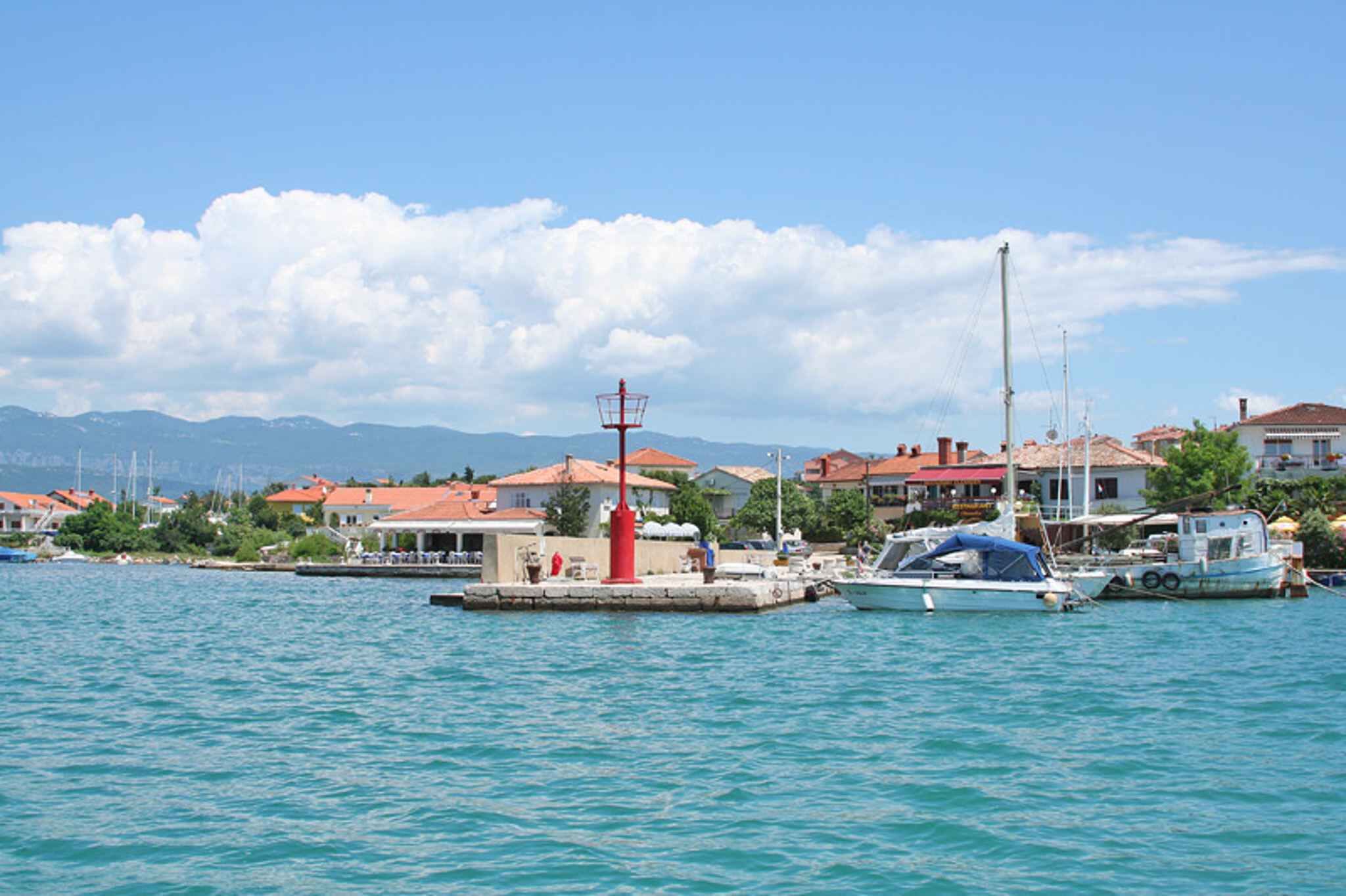 A marina with boats docked, a red lighthouse, and buildings with red roofs.