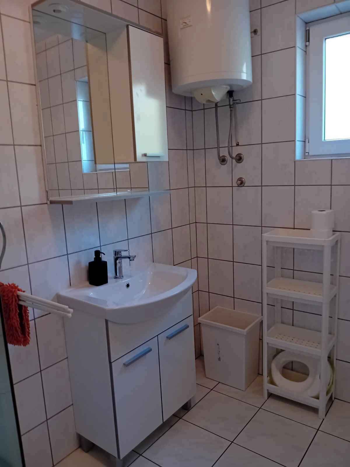 Un bany amb un rentapans blanc, un mirall i un moble, un vàter i una prestatgeria amb articles de tocador.