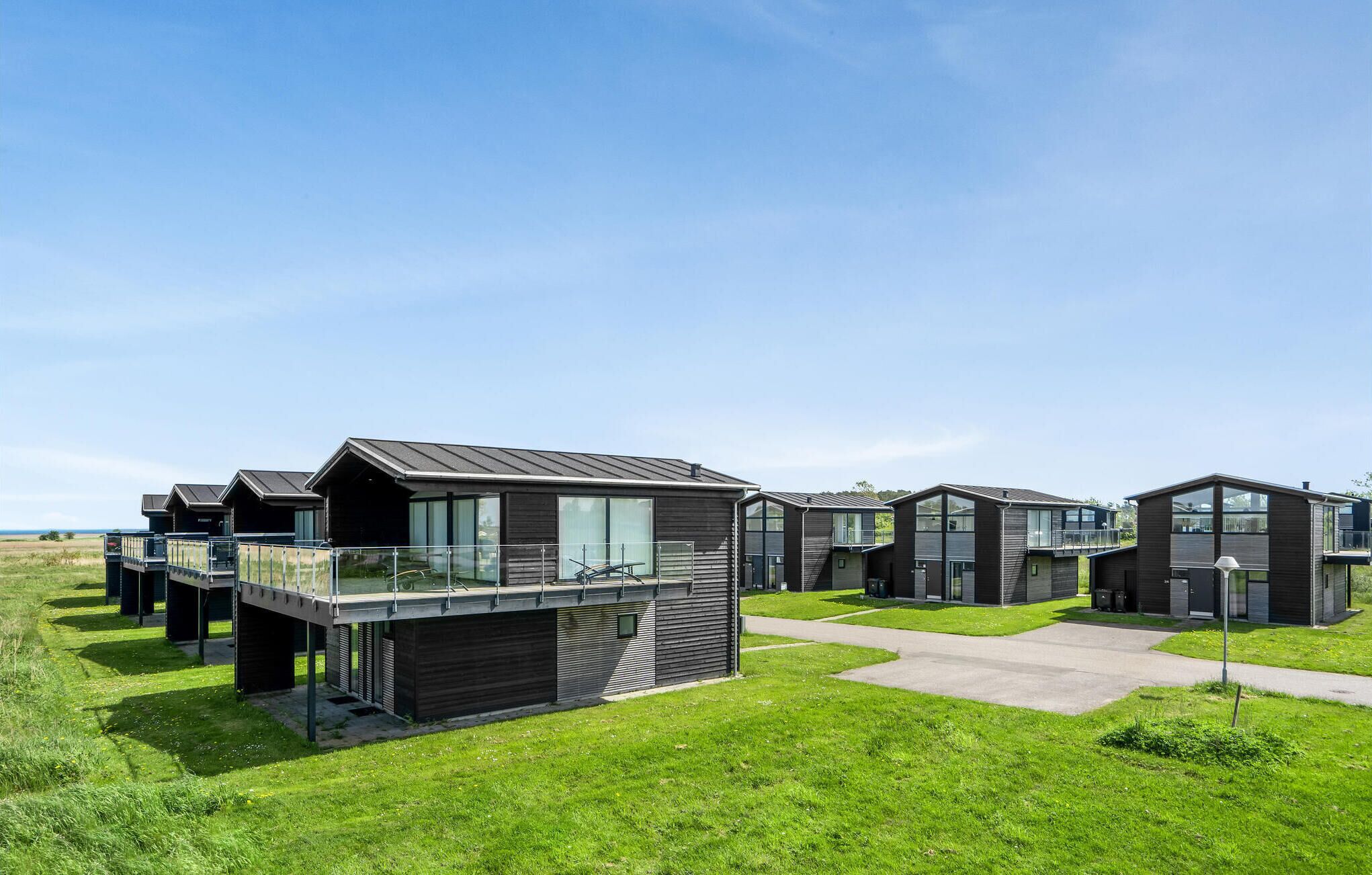 A row of modern, dark-colored cabins with balconies, set in a grassy area with clear skies.