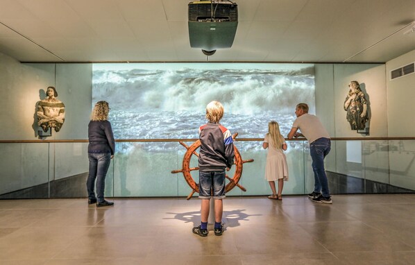 Un grupo de personas observando una proyección de un gran timón de barco en una pared de un museo.
