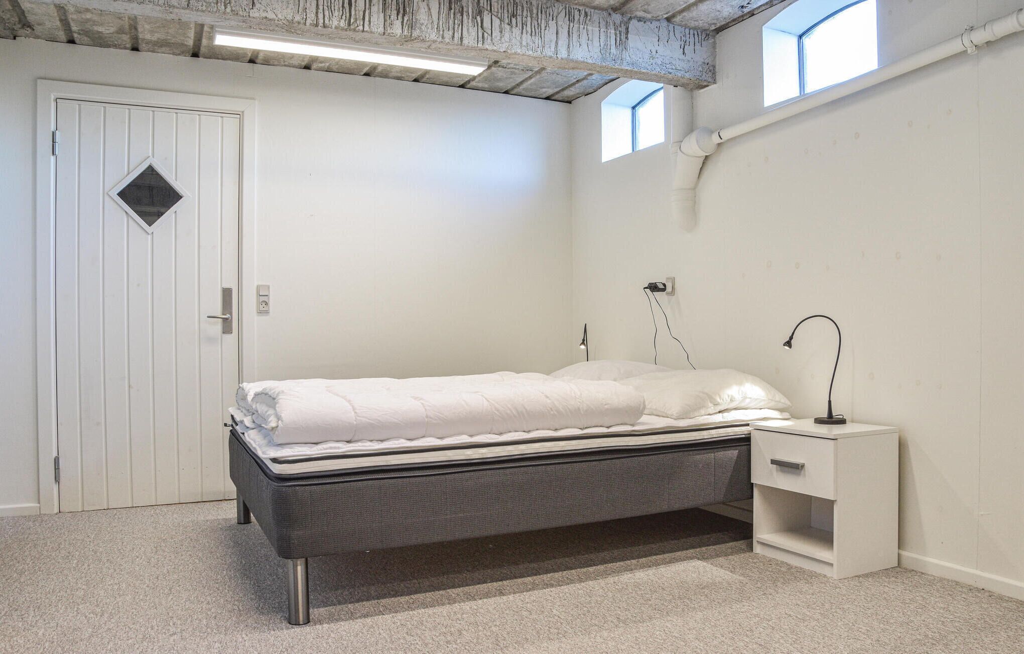 A bedroom with a bed, bedside table, lamp, and a door with a window.