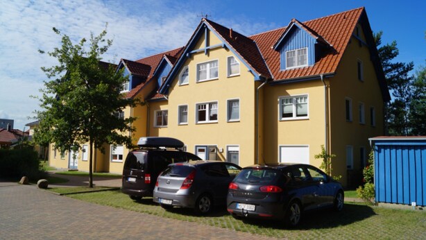 A yellow building with a red roof, parked cars, and a blue shed. - Große Kastanie 57 - between the Baltic Sea and the city center - Ferienwohnung große Kastanie (Graal-Müritz)