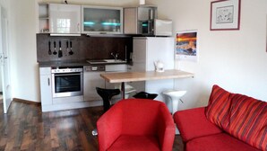 A compact kitchen with modern appliances, a dining table, and a red sofa in a living area. - Große Kastanie 57 - between the Baltic Sea and the city center - Ferienwohnung große Kastanie (Graal-Müritz)