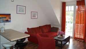 A living room with a red sofa, a coffee table with a vase of flowers, a dining table, and two framed pictures on the wall. - Große Kastanie 57 - between the Baltic Sea and the city center - Ferienwohnung große Kastanie (Graal-Müritz)