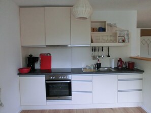A compact kitchen with white cabinets, a built-in oven, a sink, and various utensils hanging above. - 2) Holiday apartment 3-room, upper floor, 90m² - Landhaus Alte Schule near (Alt Bukow)